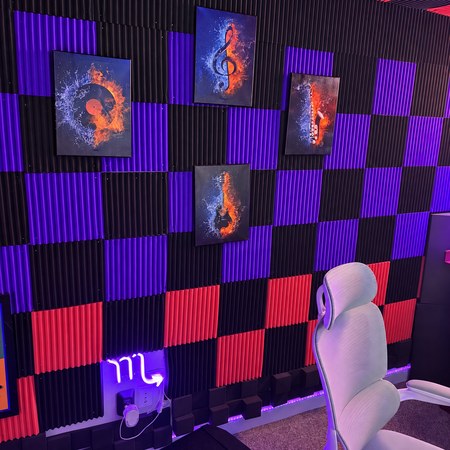 Four framed music artworks on red, black and purple acoustic panels, with a studio chair and neon light.